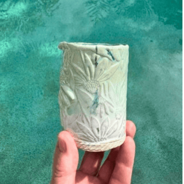 Hand holding a textured ceramic vase against a teal water background