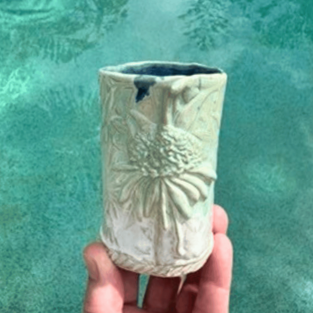 Handmade ceramic vase with textured design held against a teal background