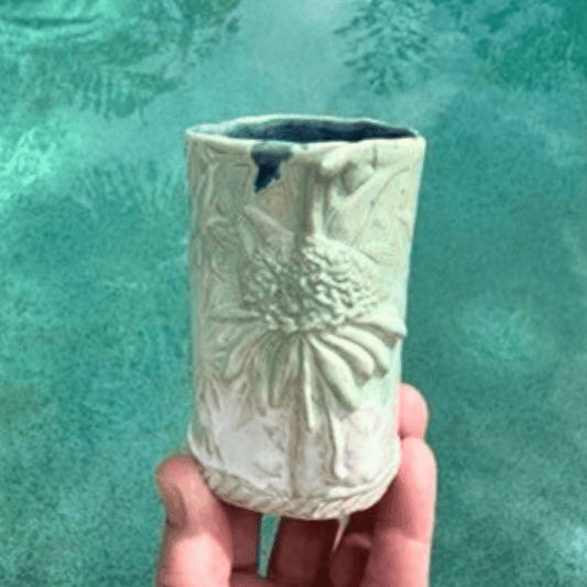 Handmade ceramic vase with textured design held against a teal background