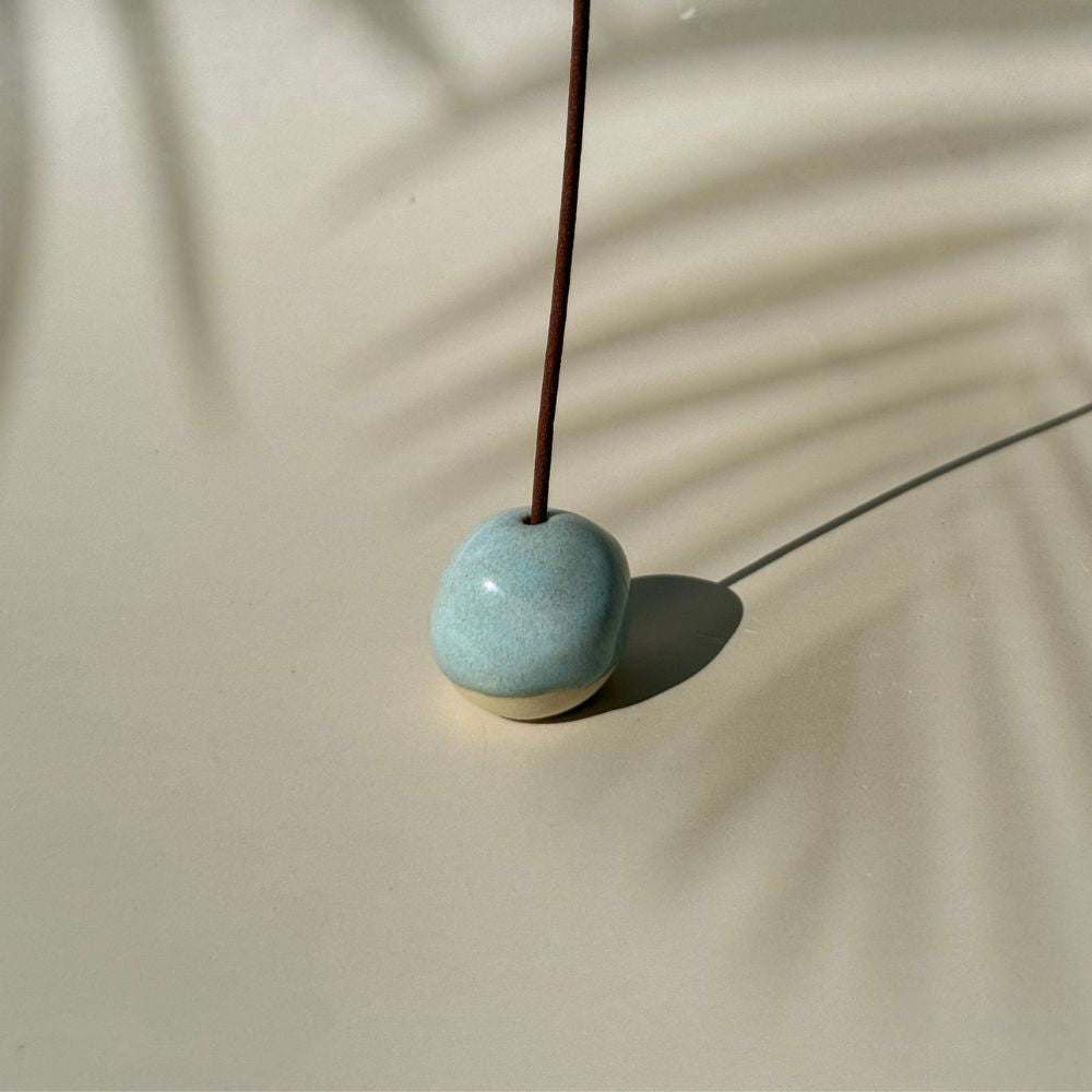 Ceramic incense holder with a single incense stick on a beige background