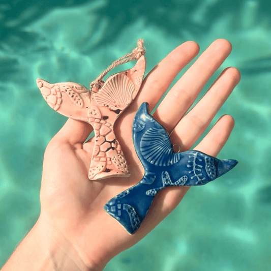 Hand holding two ceramic whale ornaments against a turquoise water background. SUnshine Pot-Tree, Sunshine Coast, Queensland, Australia