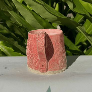Pink ceramic vase with textured design on a white surface with green leaves in the background