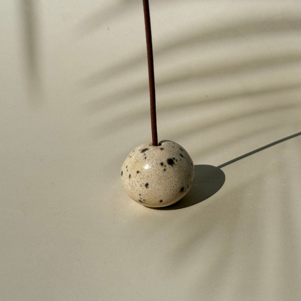 Cream Speckled Incense Pebble with a minimalist round design and black speckles, holding a single incense stick upright