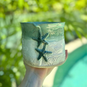 Ceramic planter with starfish design held in front of a blurred green background
