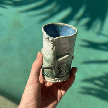 Hand holding a ceramic bud vase with a textured design against a green background