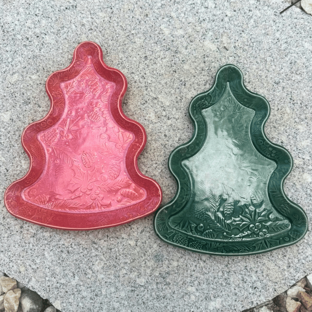 Two Christmas tree-shaped ceramic plates, one red and one green, on a concrete surface.