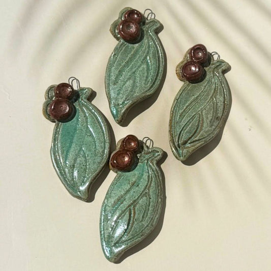 Four green ceramic leaf-shaped ornaments with brown berries on a beige background