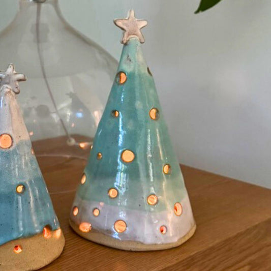 Two ceramic Christmas tree luminary cones on a wooden surface with a neutral background.