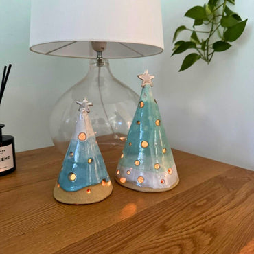 Two ceramic Christmas tree luminary cones on a wooden surface with a neutral background.