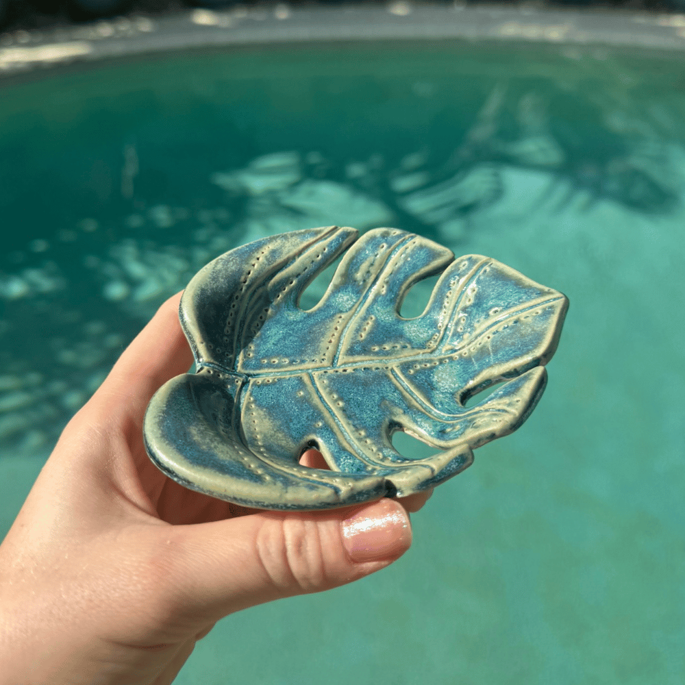 Hand holding a ceramic leaf-shaped dish with a pool in the background