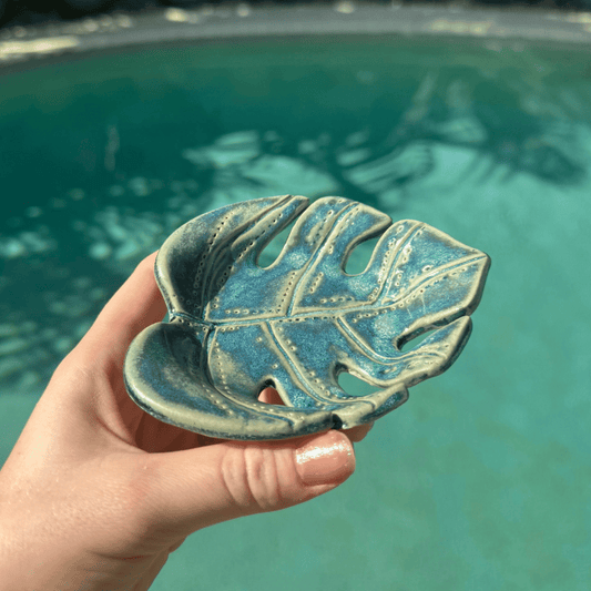 Hand holding a ceramic leaf-shaped dish with a pool in the background