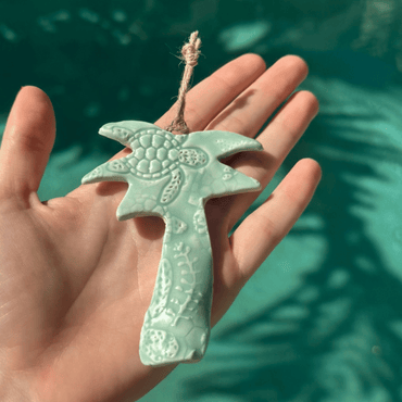 Hand holding a turquoise palm tree ornament against a blurred green background. Sunshine Pot-Tree, Sunshine Coast, Queensland, Australia