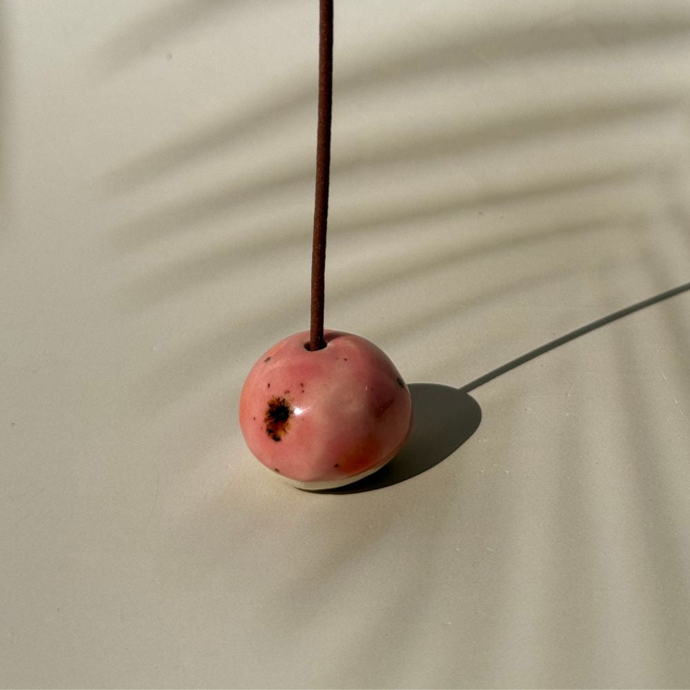 Pink ceramic incense holder with a stick on a beige background
