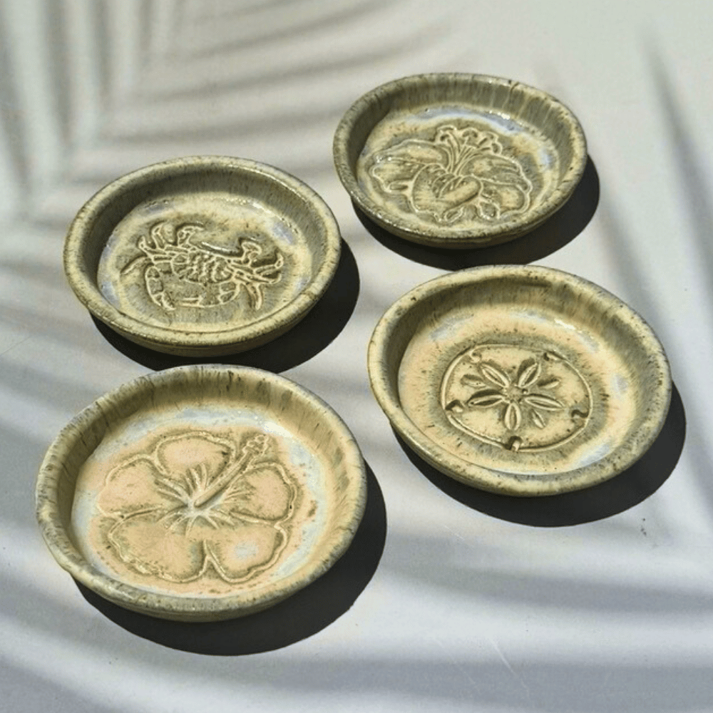 Four ceramic trinket dishes with floral designs on a textured surface