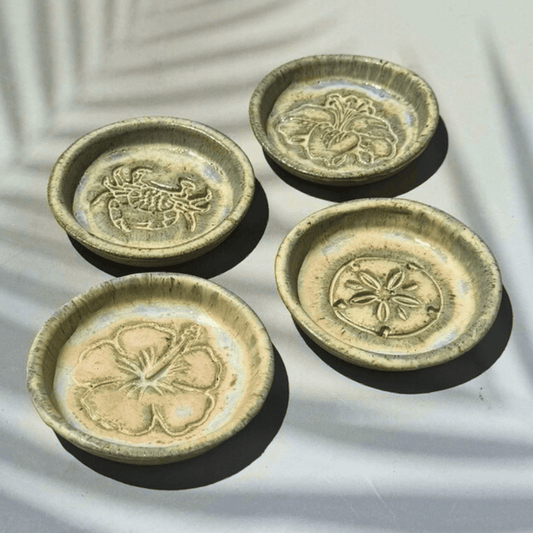 Four ceramic trinket dishes with floral designs on a textured surface