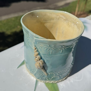 Decorative ceramic planter with shell embellishments on a white surface