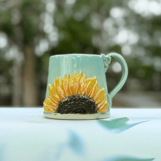 Teal mug with sunflower design on a blurred natural background