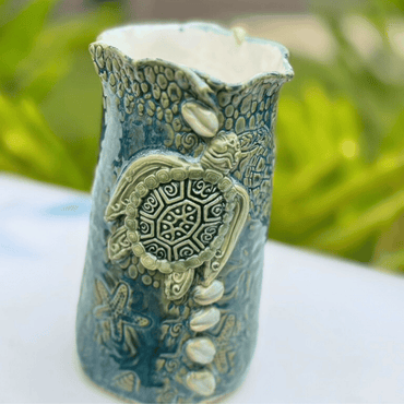 Decorative candle holder with turtle design on a white surface with greenery in the background