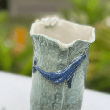 Ceramic vase with textured surface and blue accents on a blurred natural background