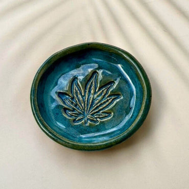 Blue ceramic dish with a cannabis leaf design on a beige background