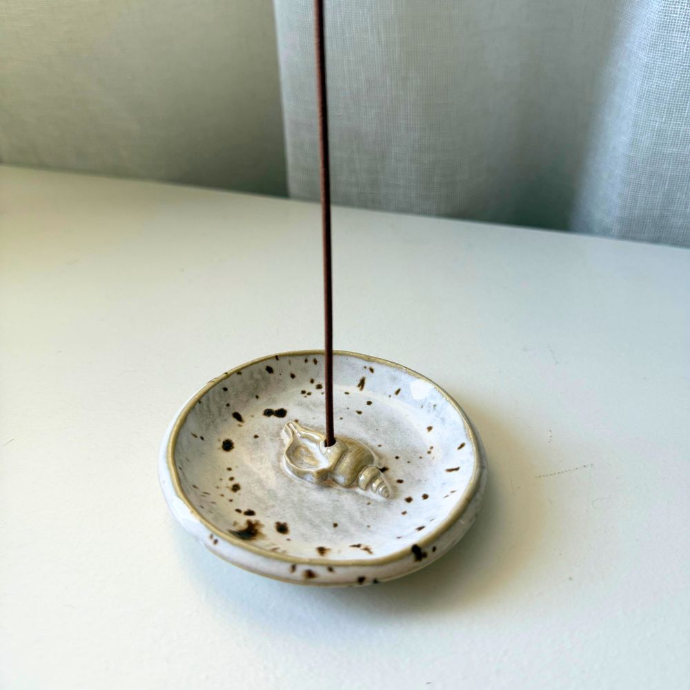 Ceramic incense holder with a single incense stick on a white surface.