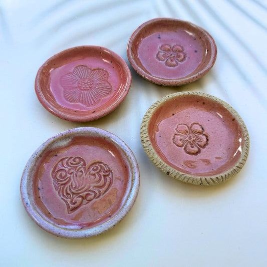 Four pink ceramic dishes with floral and heart designs on a white background