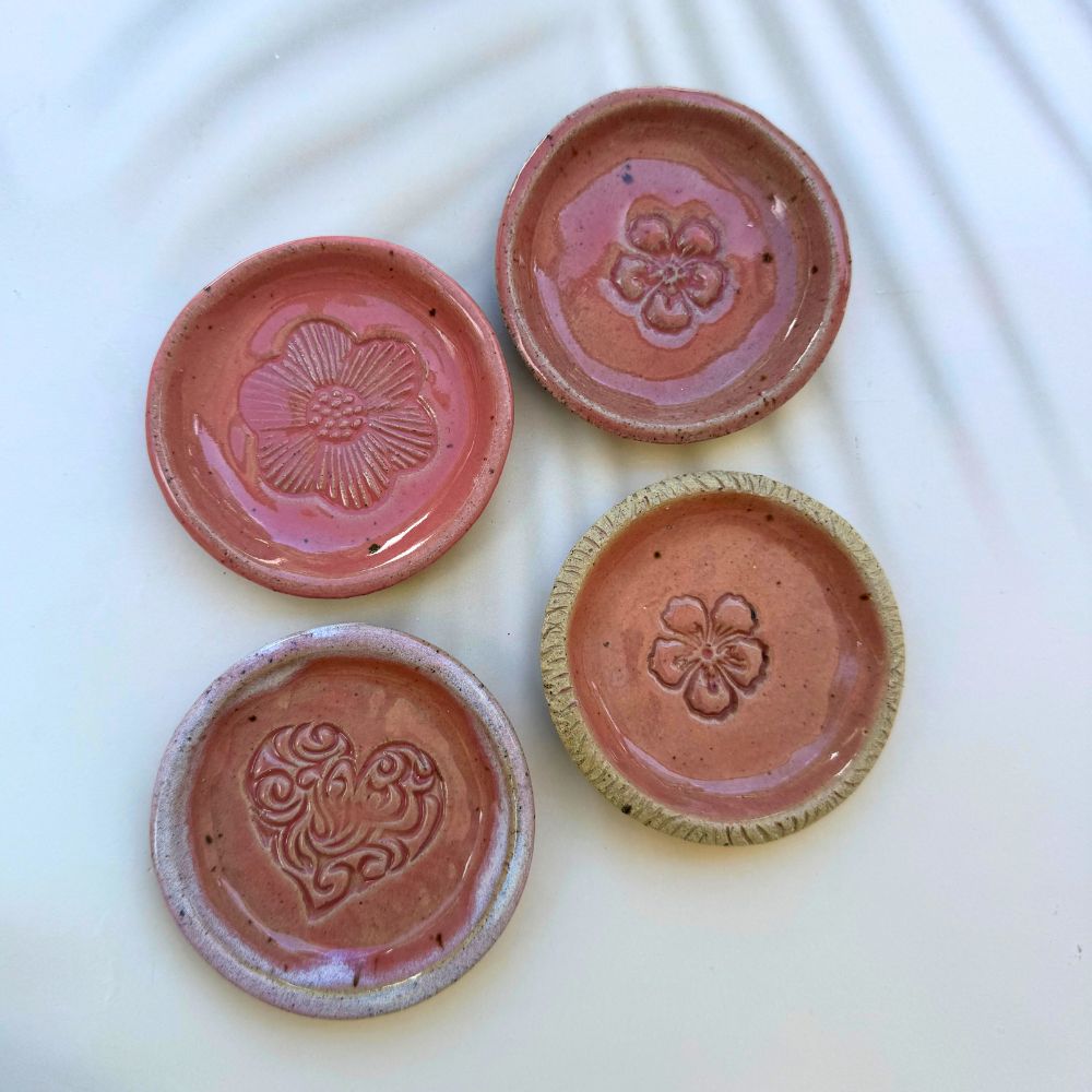 Four terracotta plates with floral and heart designs on a white background