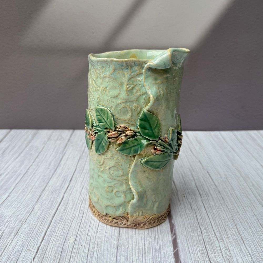 Green ceramic vase with leaf design on a wooden surface
