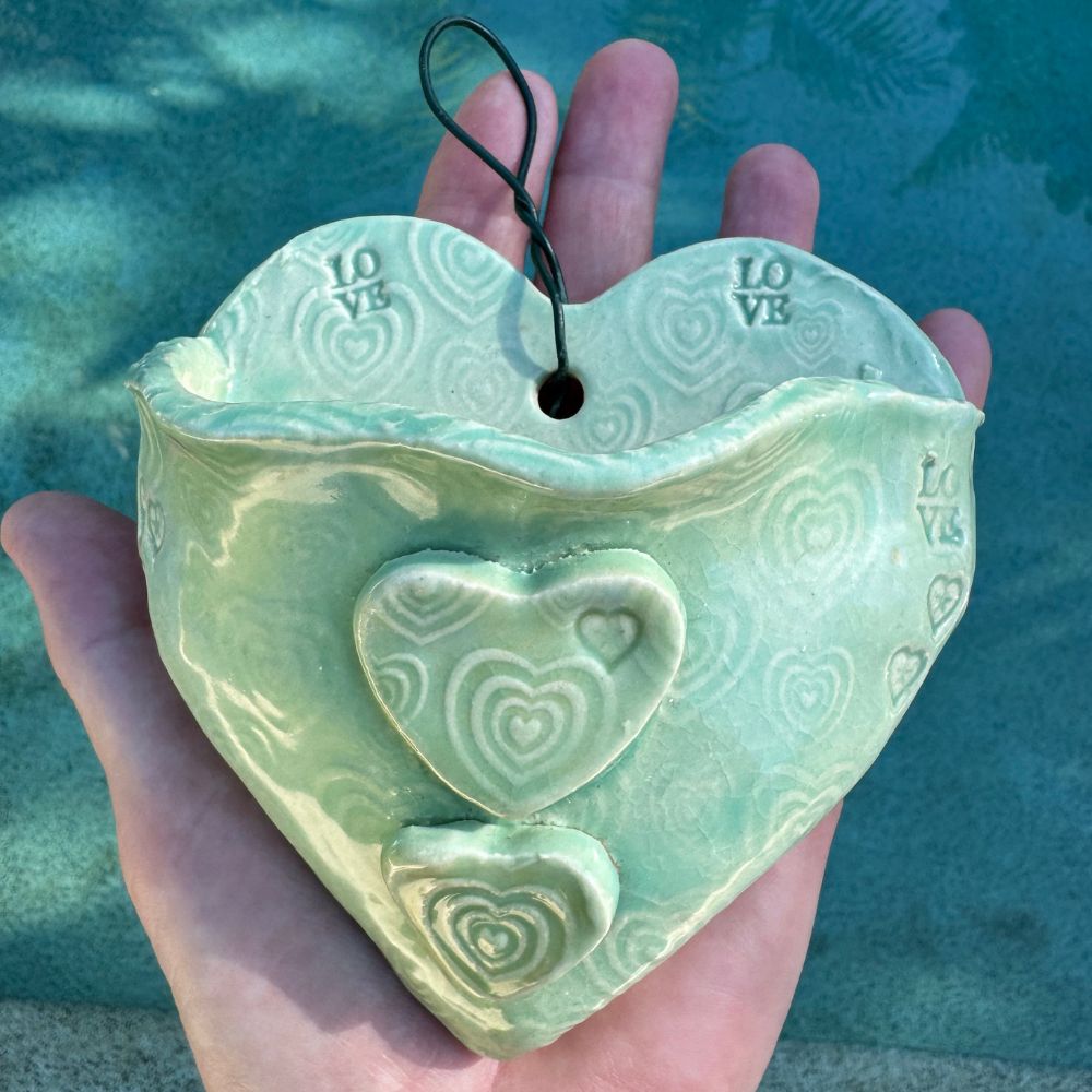Heart-shaped ceramic wall planter with embossed designs held against a blue water background