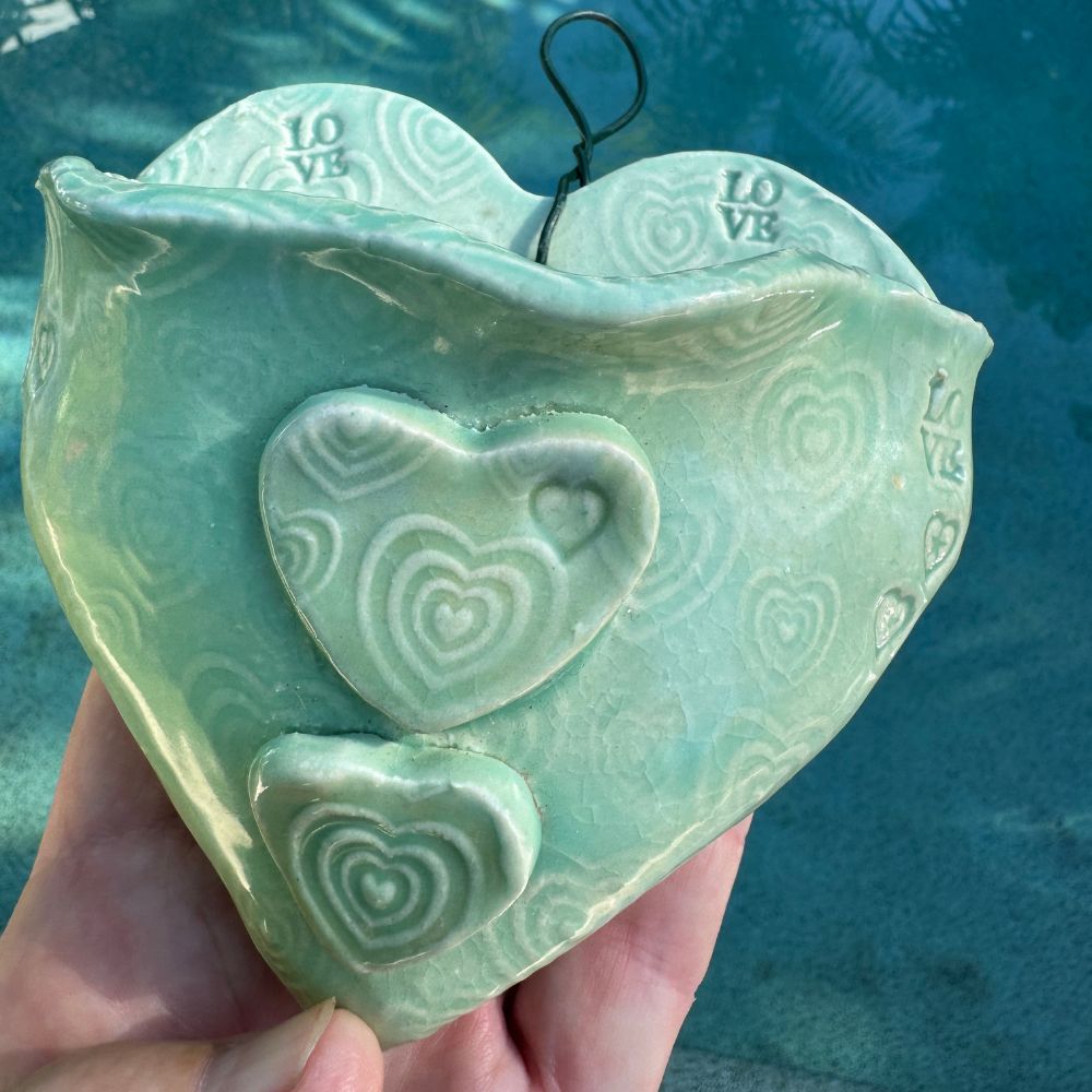 Heart-shaped ceramic wall planter with embossed designs held against a blue water background