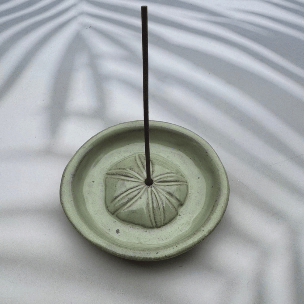 Green ceramic incense burner with a single incense stick on a light background