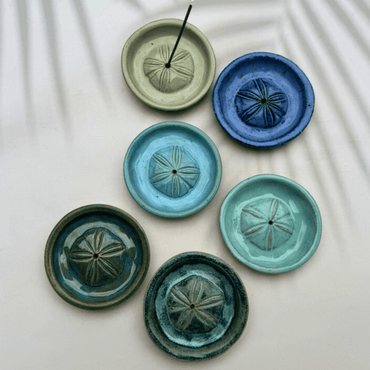 Set of six ceramic incense holders with sand dollar design in various shades of green and blue on a light background.