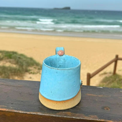 Blue ceramic cup on a wooden surface with a beach in the background