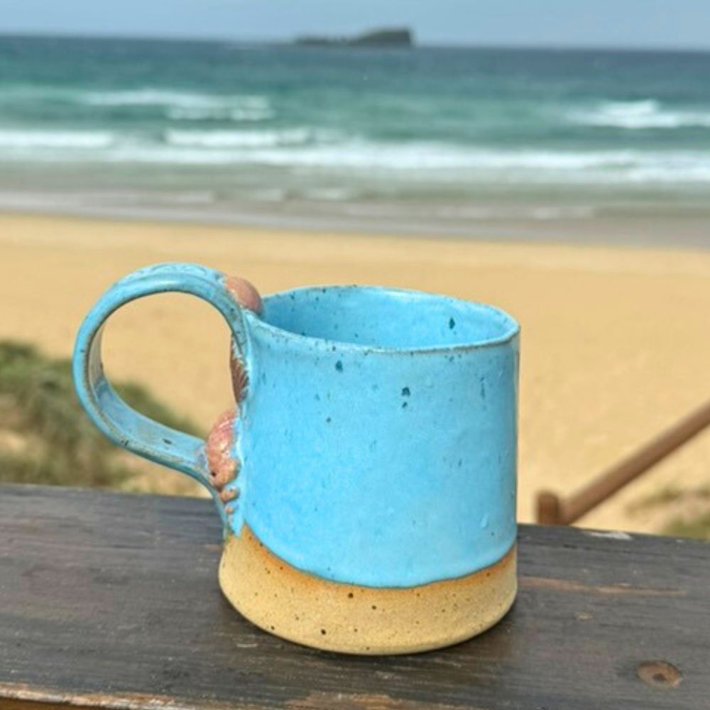 Blue ceramic mug on a wooden surface with a beach and ocean in the background