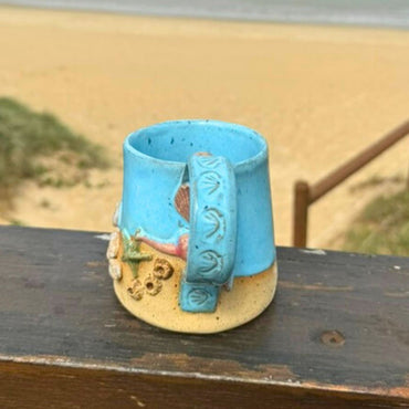 Ceramic mug with blue handle and decorative elements on a wooden surface with a blurred natural background