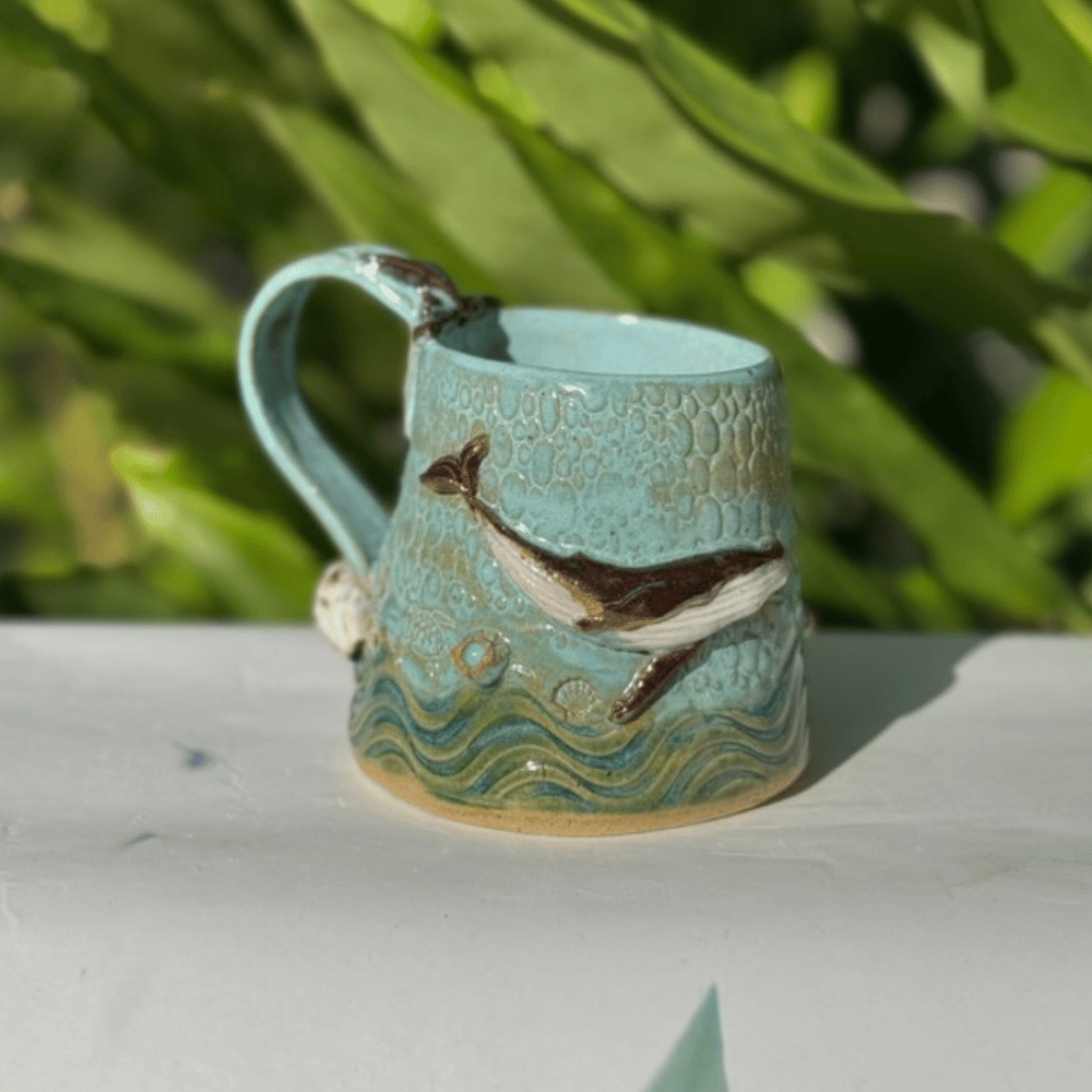Ceramic mug with whale design on a white surface with greenery in the background