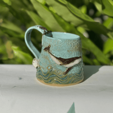 Ceramic mug with whale design on a white surface with greenery in the background