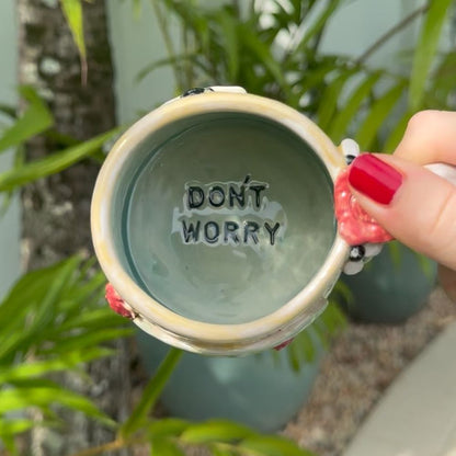 Person holding a mug with 'DON'T WORRY' text against a natural background