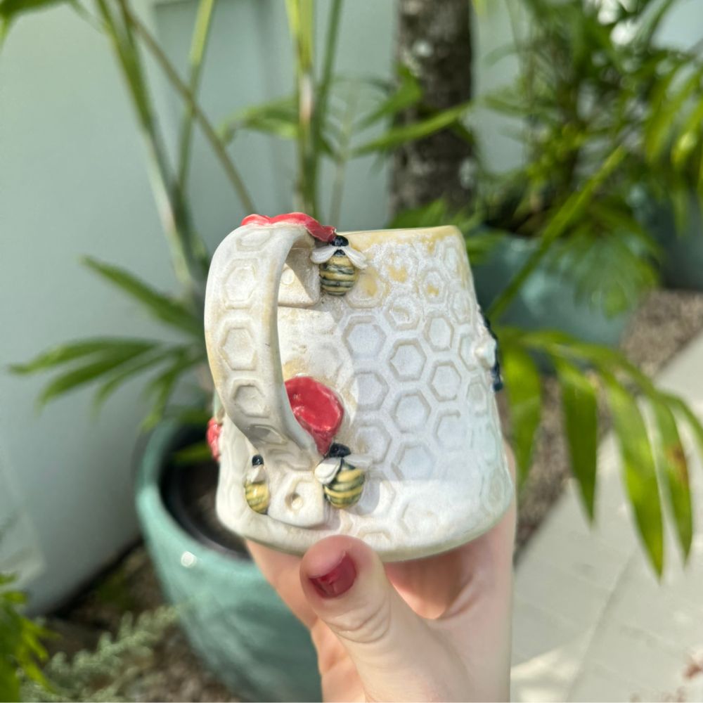 Hand holding a decorative shoe with honeycomb design and bees, plants in the background