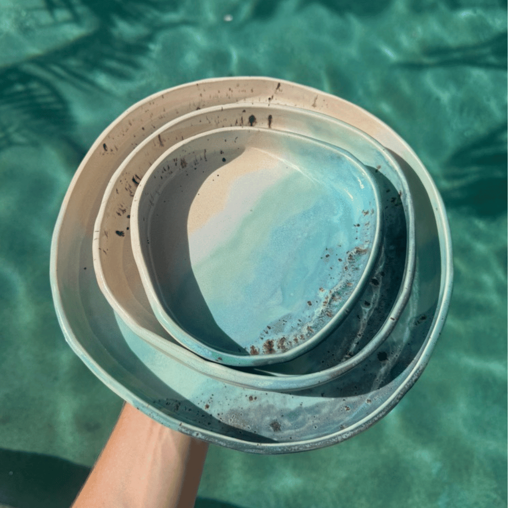 Stack of ocean glazed ceramic blates nesting bowls held over a pool with clear water.