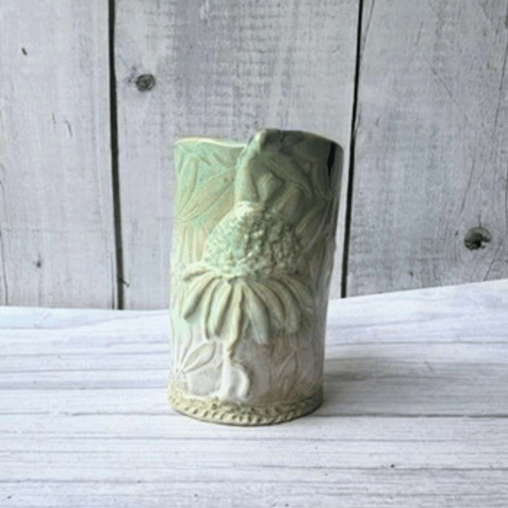 Green ceramic vase with floral patterns on a wooden surface
