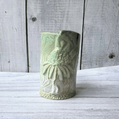 Green ceramic vase with floral patterns on a wooden surface