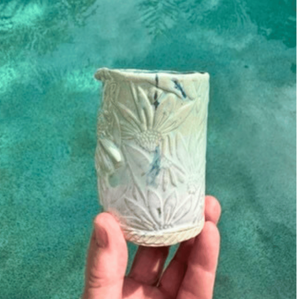 Hand holding a textured ceramic vase against a teal water background