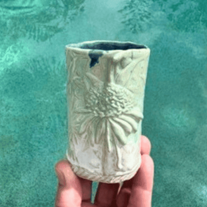 Handmade ceramic vase with textured design held against a teal background