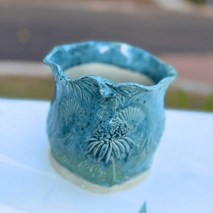 Blue ceramic planter with floral patterns on a white surface