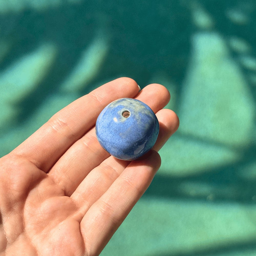 Hand holding a blue incense bead with a blurred green background