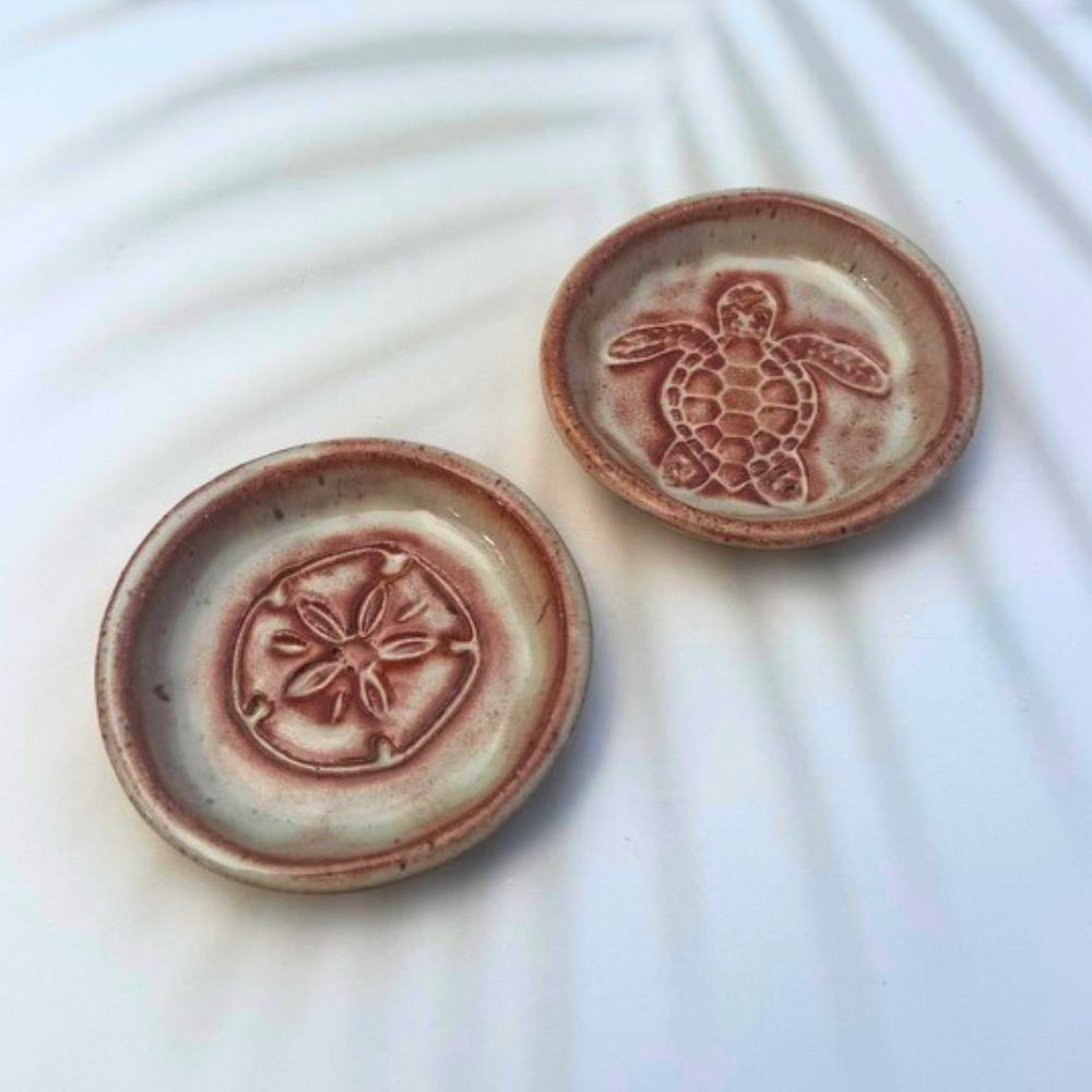 Two ceramic trinket dishes with turtle and sand dollar designs on a white background