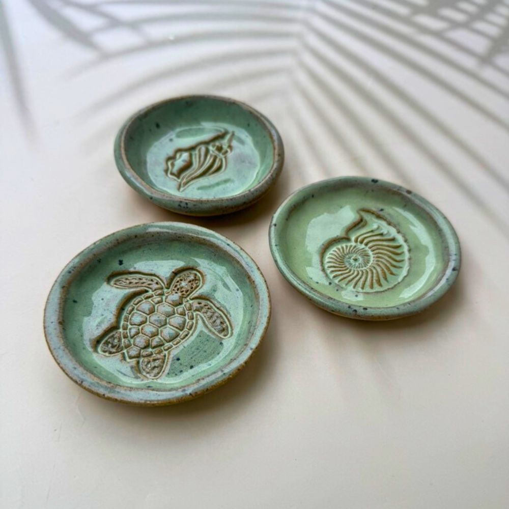 Three green ceramic dishes with embossed designs on a light background