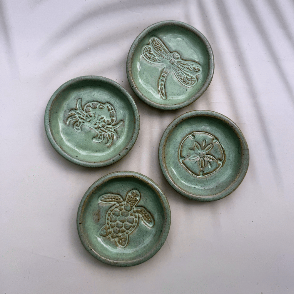 Four ceramic coasters with animal embossments on a white fabric background