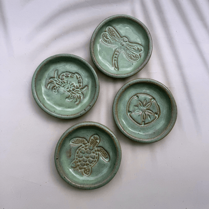 Four ceramic coasters with animal embossments on a white fabric background